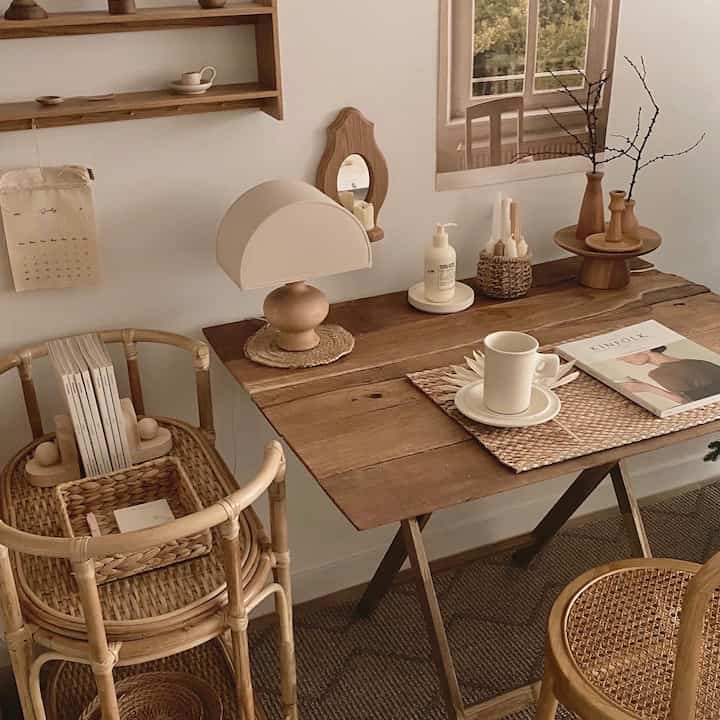 Natural color tone home office space featuring a wood table, rattan chairs, table lamp, and mug with a warm, cozy atmosphere