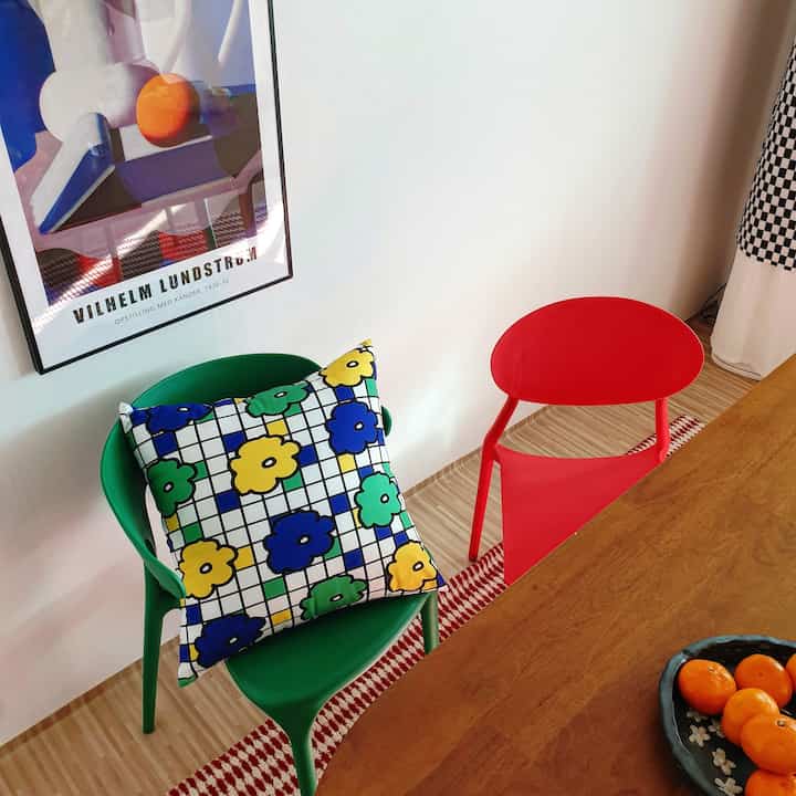 Dining area featuring red and green chairs with a colorful patterned cushion and wall poster creating a bright accent interior
