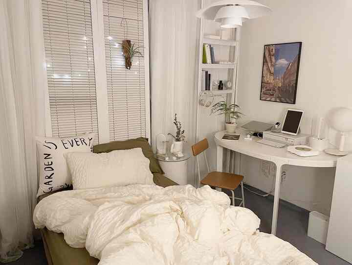Warm beige and white toned studio bedroom featuring bed, desk, and plants with a simple, natural atmosphere