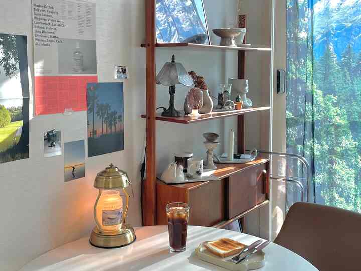 暖かいウッドトーンと白の調和があるリビング、ヴィンテージキャビネットとテーブルランプ、ポスターが配された雰囲気のあるカフェ風インテリア