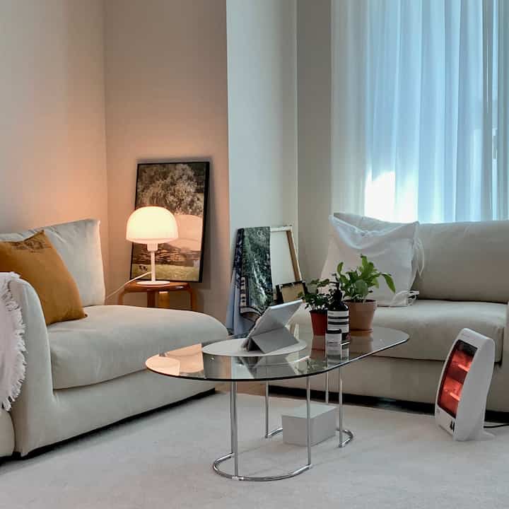 アイボリー調のリビング、2つのモダンソファとガラスのコーヒーテーブル、植物とテーブルランプが配置された落ち着いた雰囲気のインテリア