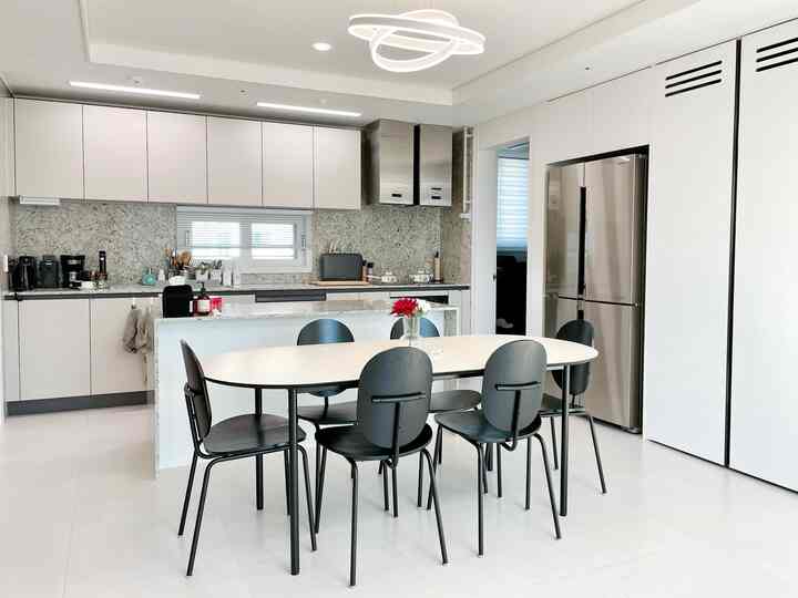 白と黒のトーンのキッチン、中央に6人用ダイニングテーブルと椅子が配置された洗練されたモダンな空間