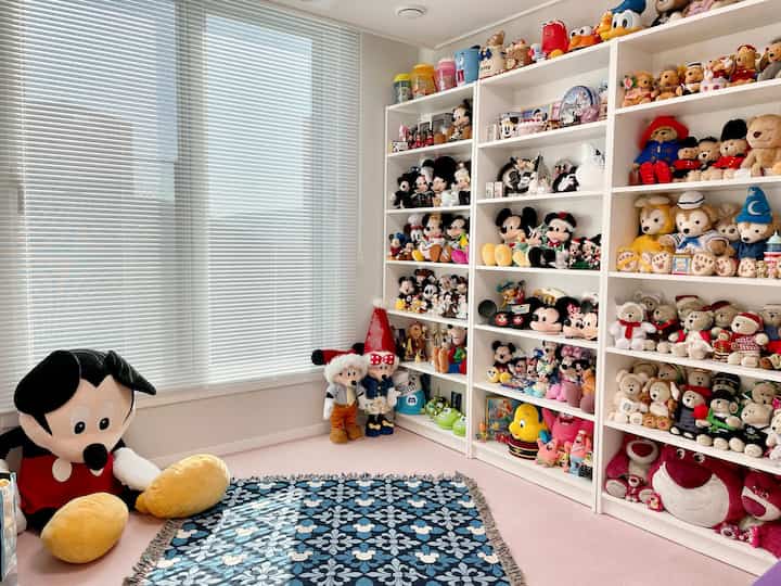 White and black toned adult hobby room filled with Disney plush toys and bookshelves in a clean layout