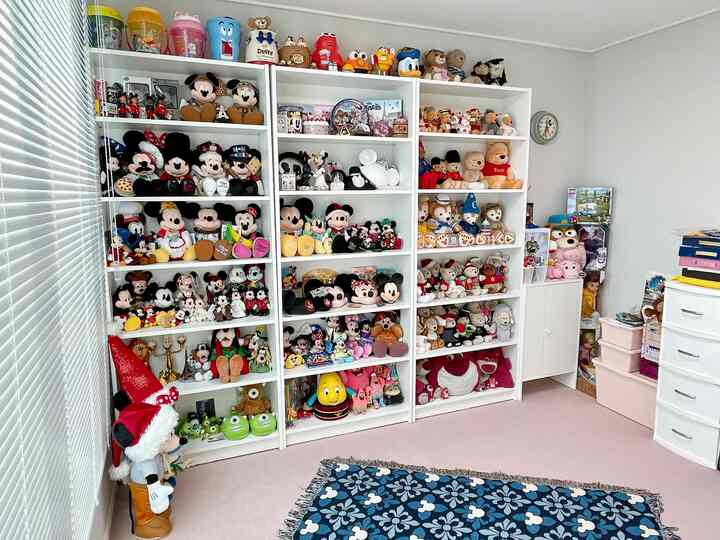 Warm and cozy room with light gray walls and white bookshelves filled with Disney plush toys including Mickey Mouse