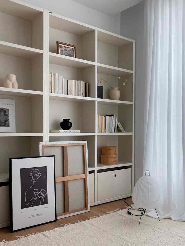 A natural modern study space in white and beige tones featuring a bookshelf, picture frames, vases, and a rug arranged neatly