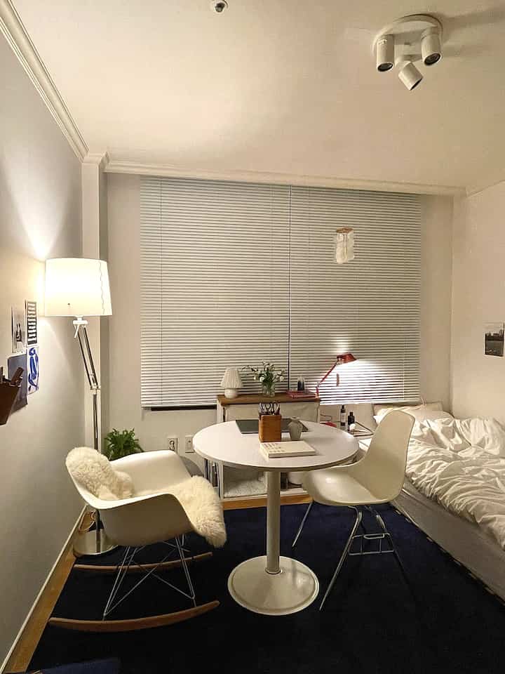 ホワイトとネイビー調の寝室、丸テーブルとアームチェア、ブラインドが配置された雰囲気のあるモダンヴィンテージ空間