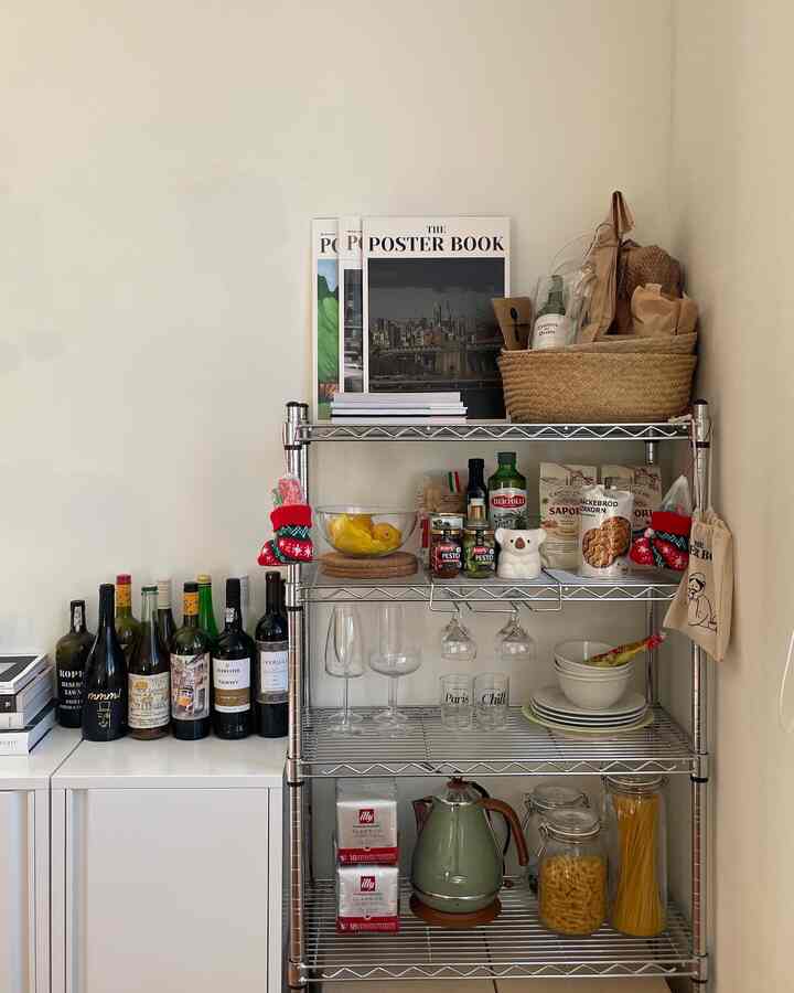 Ivory-toned kitchen space featuring a stainless steel rack holding wine glasses, baskets, Illy coffee capsules, and organized storage against a white cabinet backdrop