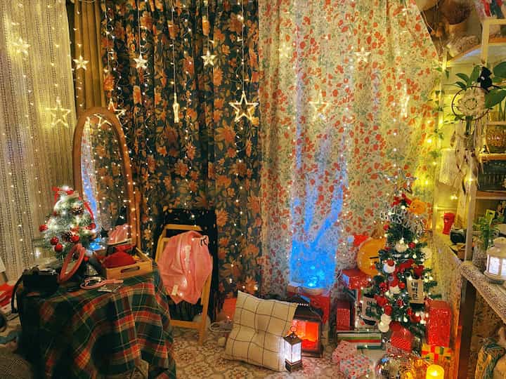暖かい黄色の光とヴィンテージの花柄カーテンが調和したクリスマス装飾と照明のある居心地の良い空間