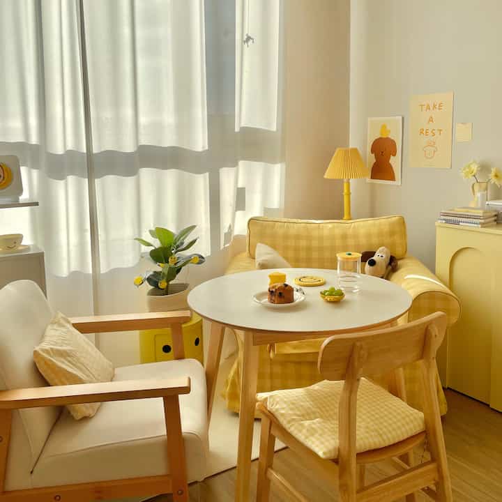 Warm yellow-toned studio living room featuring wooden furniture, a home cafe table, and a dog plush for cozy ambiance