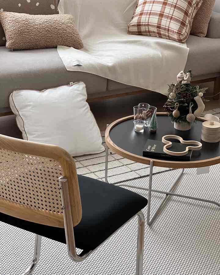 ベージュと黒のトーンのリビング、ラタンチェアと丸いコーヒーテーブル、ミニクリスマス装飾が配置された温かみのあるモダンなインテリア