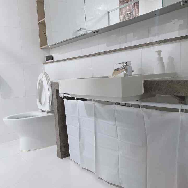 White tiled bathroom featuring a sink with exposed pipes concealed by a white curtain, creating a clean look