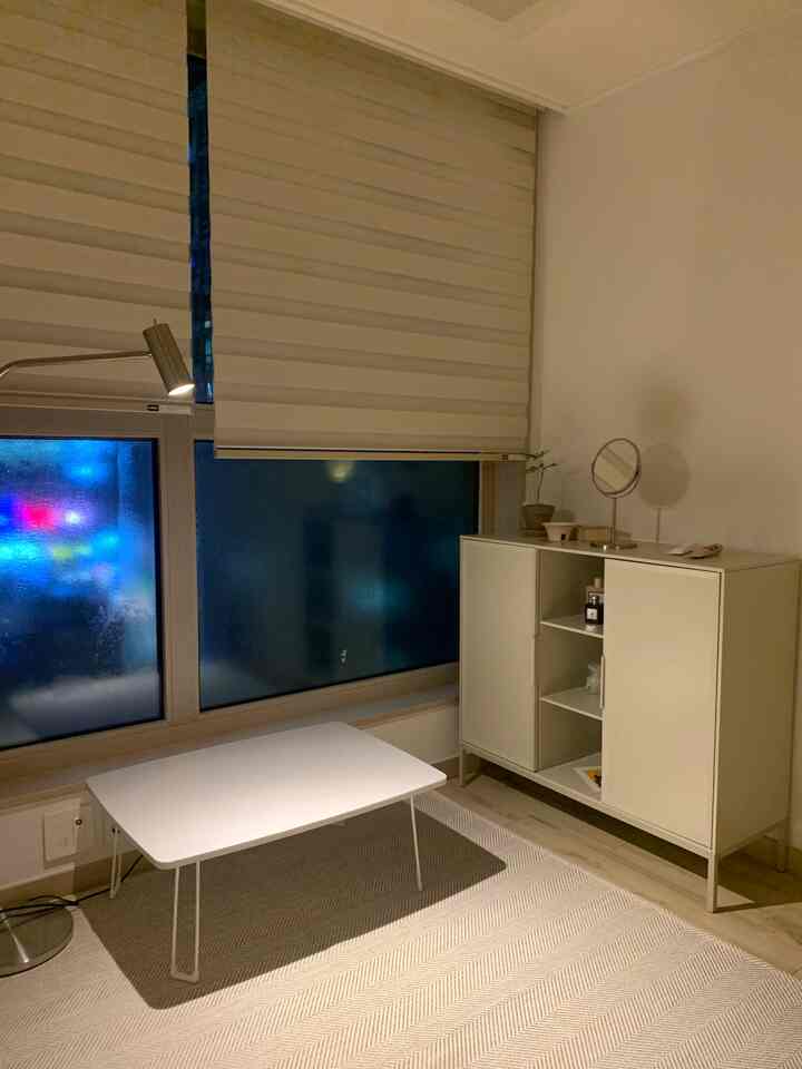 A compact studio apartment living room in white and beige tones, featuring a side table and storage cabinet with a clean modern atmosphere