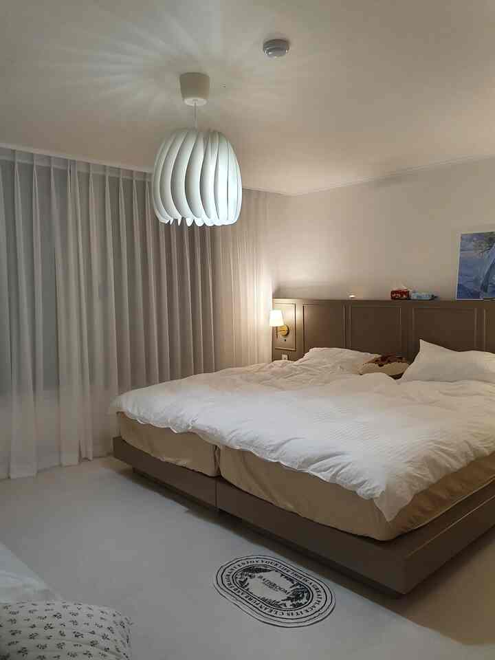 ライトグレーとホワイトの寝室、ホテルライクなベッド、レースカーテン、ペンダントライトが配置された落ち着いた雰囲気のインテリア