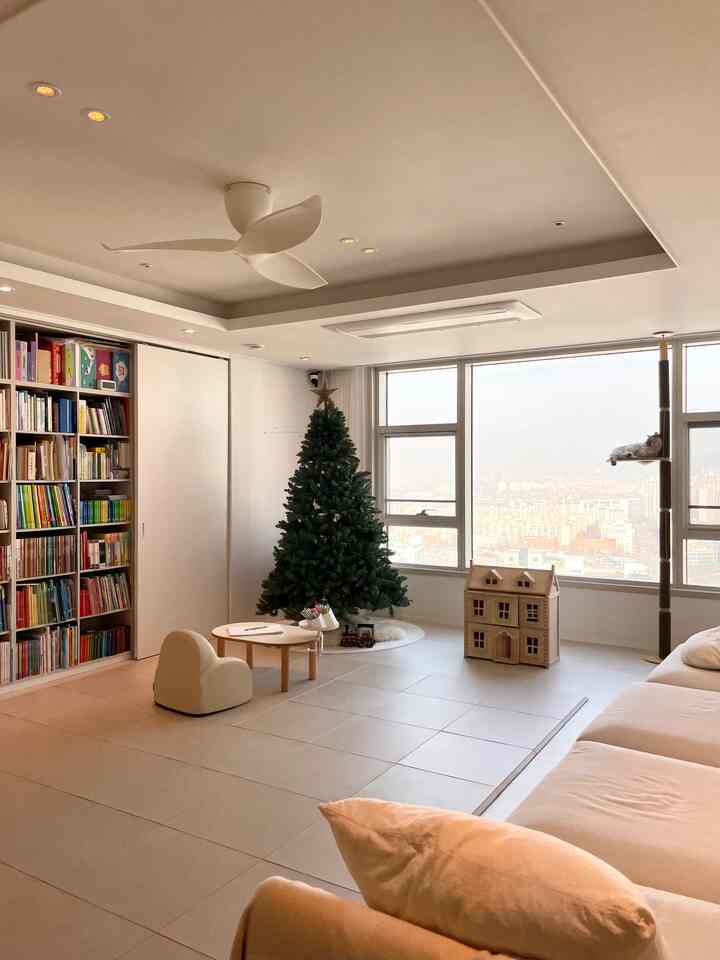 Beige and white toned living room featuring large bookshelf, cat tower, and kids' furniture in a clean natural space