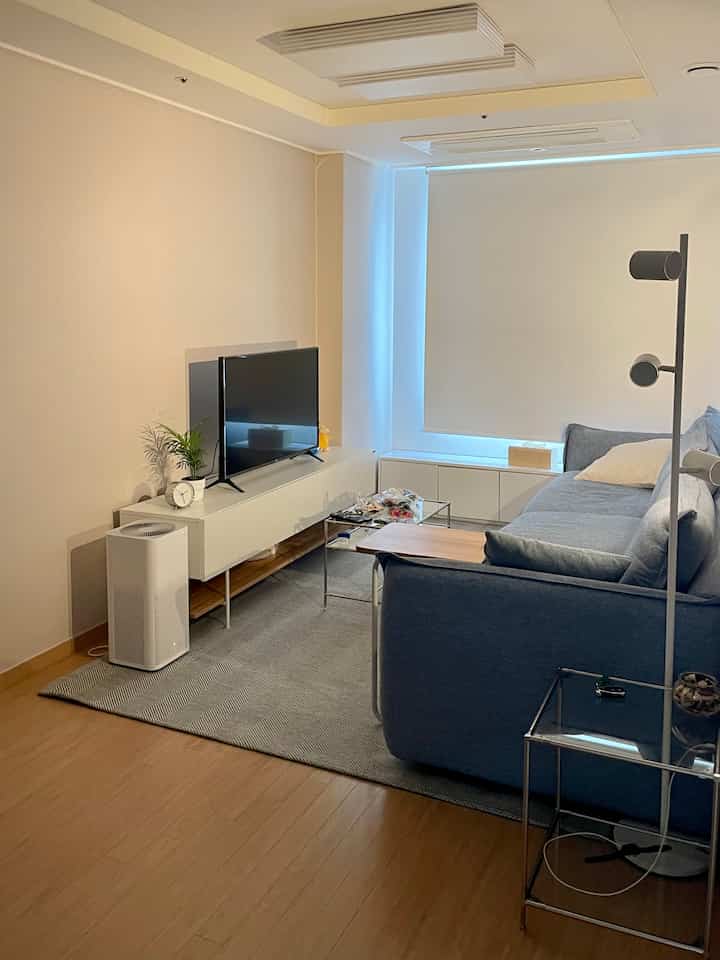 Modern living room with white and wood tones, featuring a blue sofa and TV stand in a clean setting