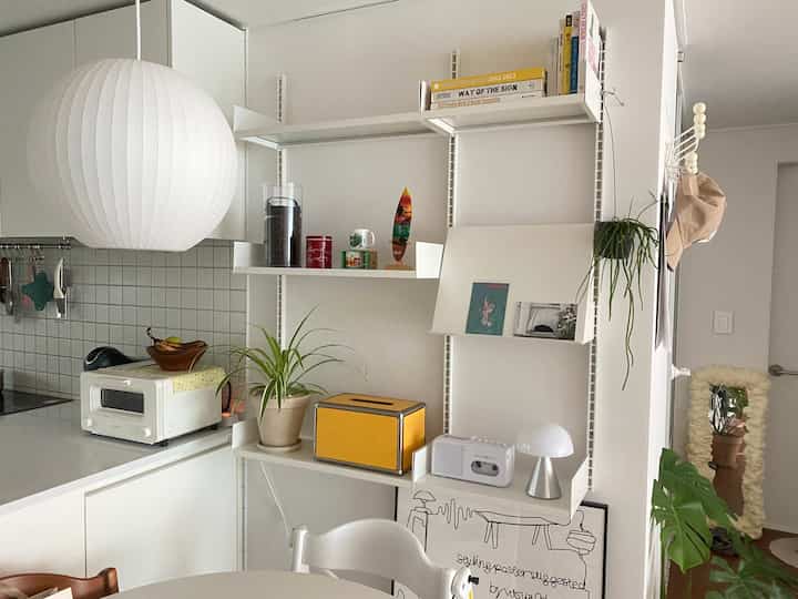 ホワイトトーンのキッチン、システム棚と多様なオブジェが配置された清潔で自然な雰囲気のインテリア