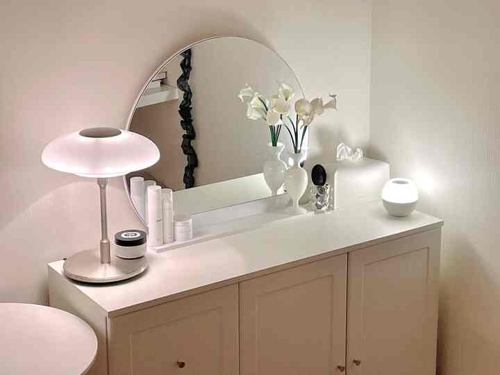 White-toned vanity with round mirror, lamps, and vases arranged in a clean and elegant interior space
