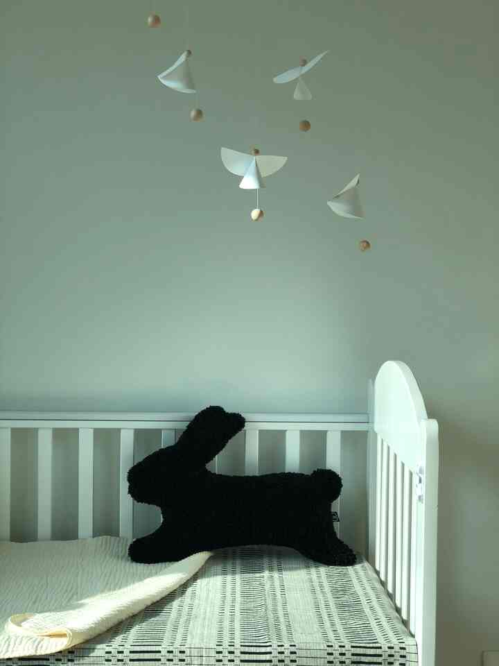 White-toned kids' room featuring angel mobile and black bunny cushion, creating a cozy and simple atmosphere