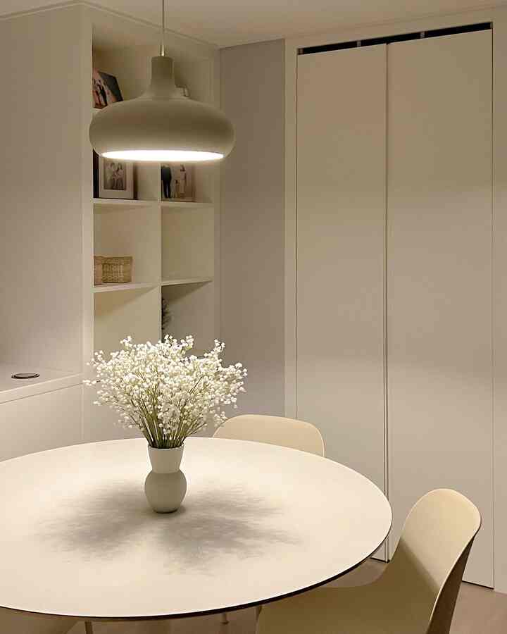 白を基調としたキッチン・ダイニング、円形テーブルとペンダントライト、造花が調和したシンプルな空間