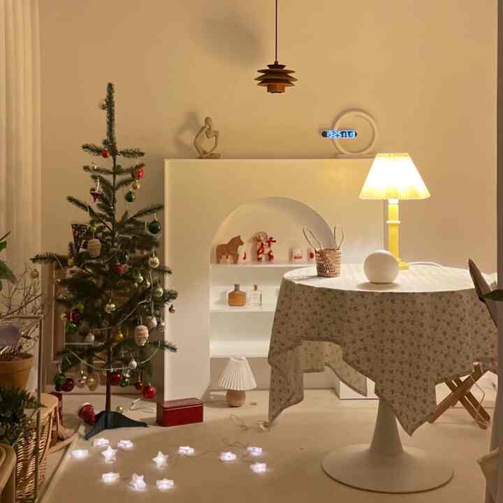 暖かいベージュとホワイトのトーンのリビング、丸テーブルに黄色いテーブルランプとクリスマスツリーが配置された雰囲気のあるインテリア