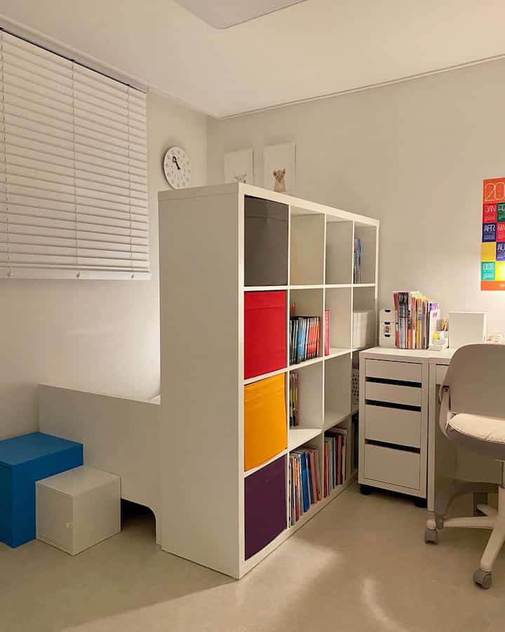 明るい白色の子供部屋、カラフルな収納ボックスを配した本棚の間仕切り、ベッドとデスクが整然と配置された清潔感のある空間