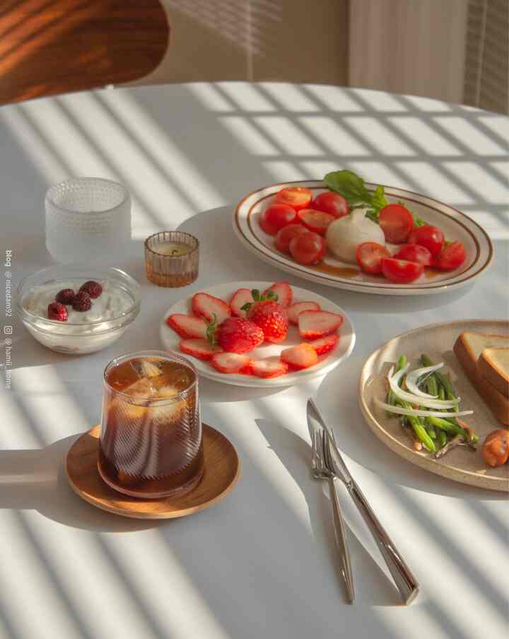 Bright white table bathed in warm sunlight decorated with various home cafe brunch plates and transparent glassware in a simple setting