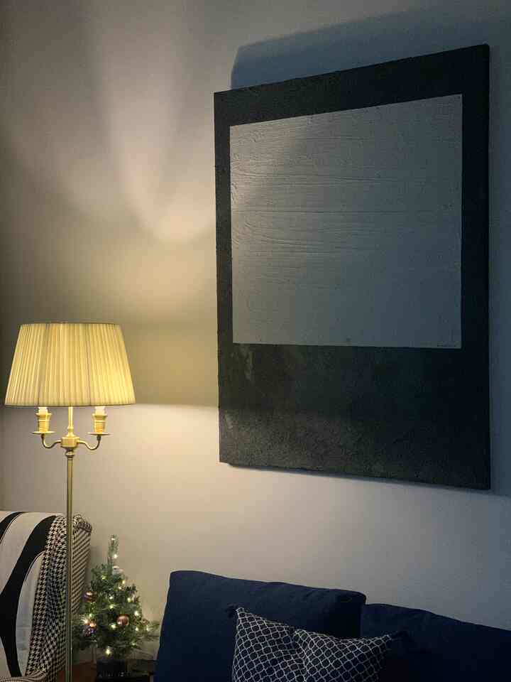 Gray-walled living room featuring a navy sofa, floor lamp, and large framed artwork creating a cozy atmosphere