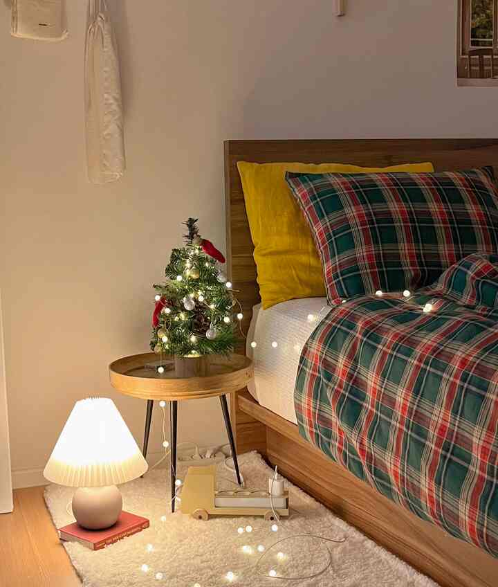 Natural tone wood bedroom featuring a Christmas mini tree and string lights creating warm ambiance