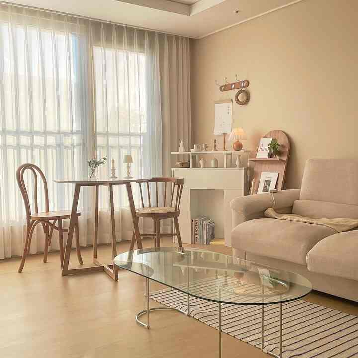 Ivory and natural-toned living room with glass coffee table and wooden dining chairs creating a cozy, warm home cafe space