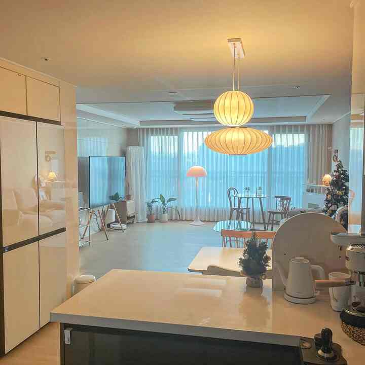 Bright white-toned kitchen and living room space featuring wooden dining chairs and pendant lighting in a simple modern interior