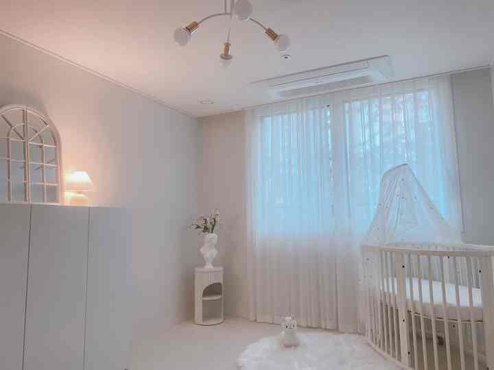 White-toned kids' room featuring a round crib and thick lace curtains creating a soft atmosphere