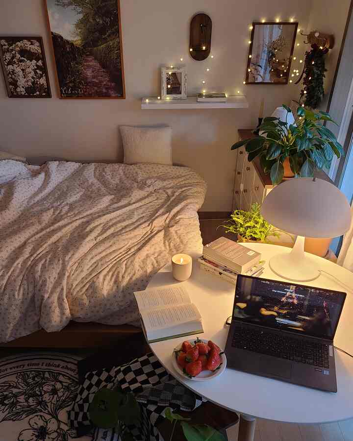 White and natural tone bedroom featuring a bed, books, laptop on a table and candle creating a warm atmosphere