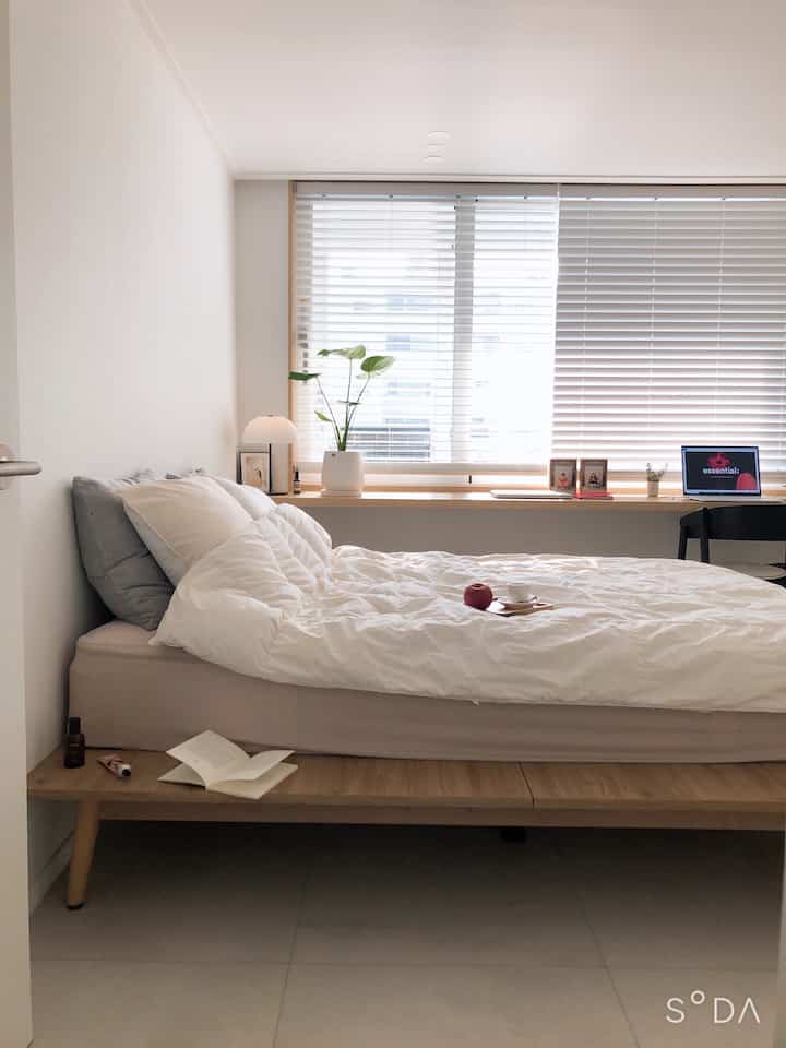 Natural tone bedroom featuring a no-headboard platform bed and wood-tone window blinds in a clean layout