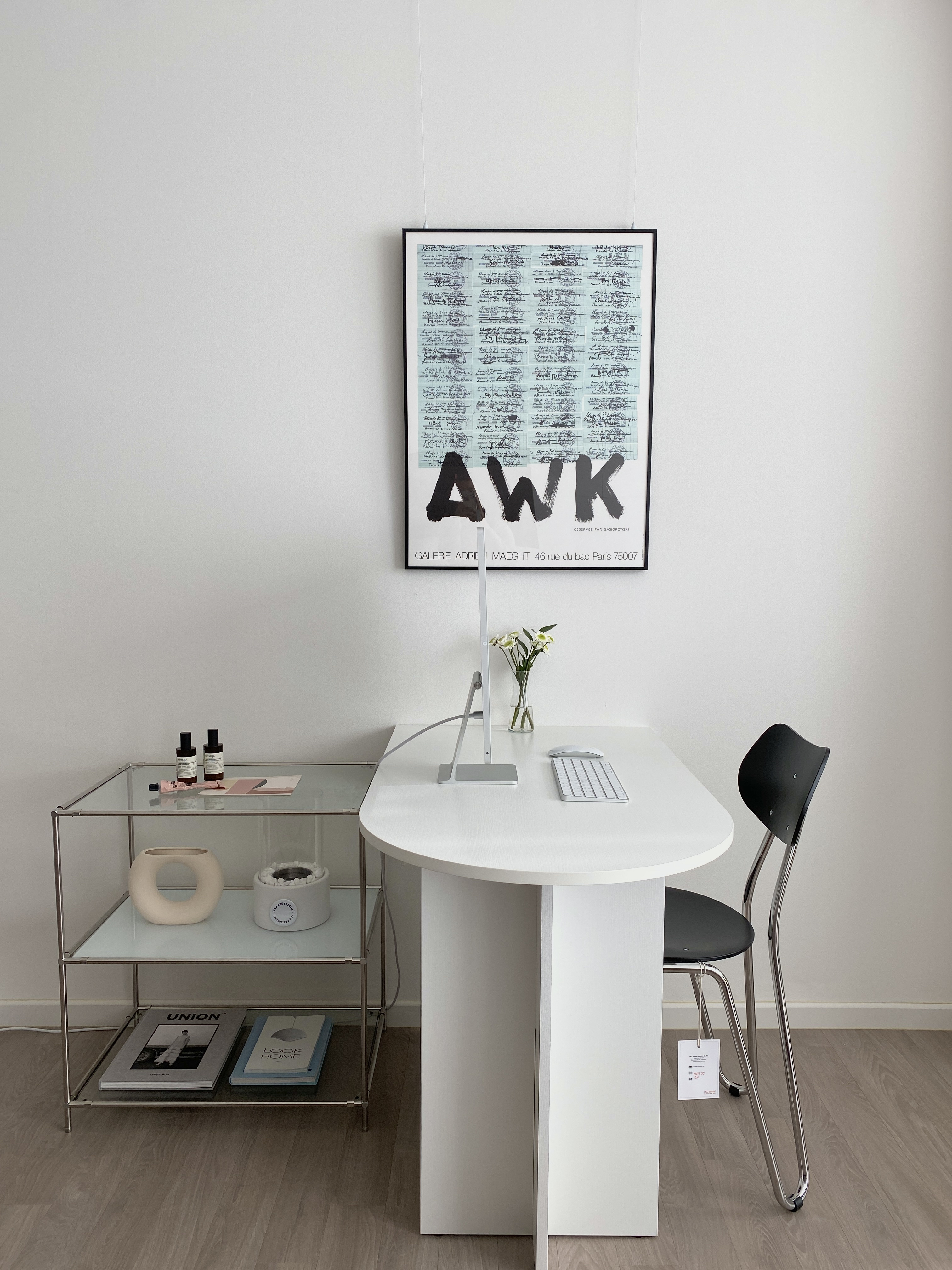 白を基調としたホームオフィス、白いデスクと黒い椅子、壁にポスターが配置されたシンプルでモダンなインテリア