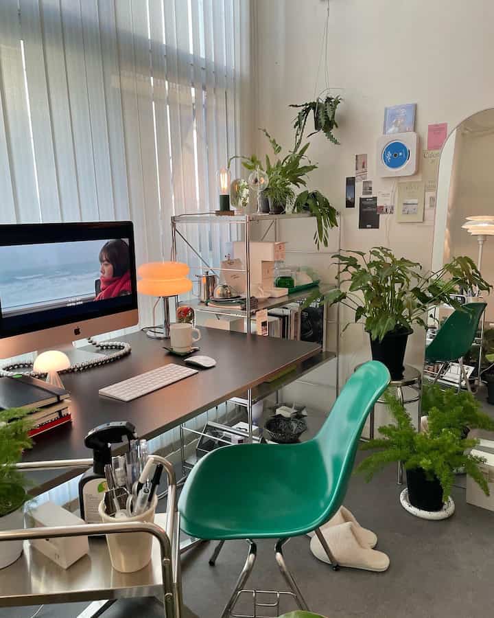A modern study-style home office in black and green tones with an Eames chair, Muji shelving, and several plants creating a fresh, tidy atmosphere