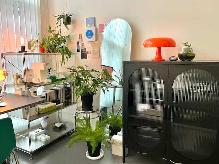 ブラックの金属キャビネットとオレンジ色のアルテミデランプがあるナチュラルなプランテリアリビングルーム