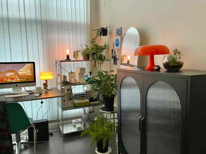 Bright white-walled home office featuring black metal shelves and storage cabinet, complemented by green plants and warm lighting for cozy ambiance
