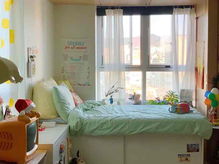 A cozy small bedroom in white and light green tones, featuring a storage bed by the window with baby plush toys
