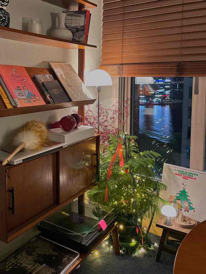 暖かい木のトーンと緑の植物が調和した居心地の良いホームオフィス空間、窓際にクリスマスツリーが配置されている