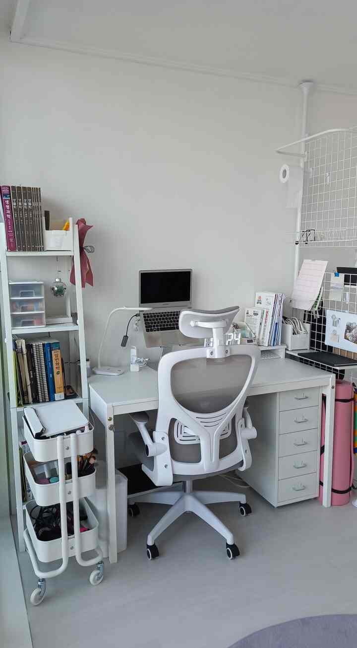 White-toned compact home office featuring a white desk, ergonomic chair, and organized shelves with books and supplies