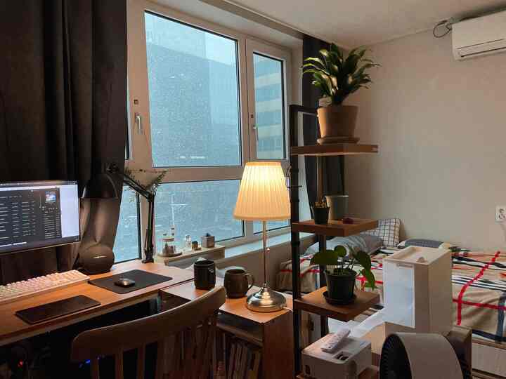 白い壁と木製家具が調和した一人暮らしのワンルーム、雪が降る窓の景色とホームオフィスのある居心地の良い空間