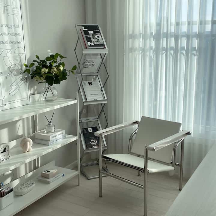 Bright white-toned study space featuring a white chair, shelves, and magazine rack with a clean and natural atmosphere