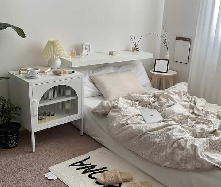 ホワイトとベージュの色調の寝室、白いベッドとチェック柄の掛け布団が温かみのある雰囲気を演出するインテリア