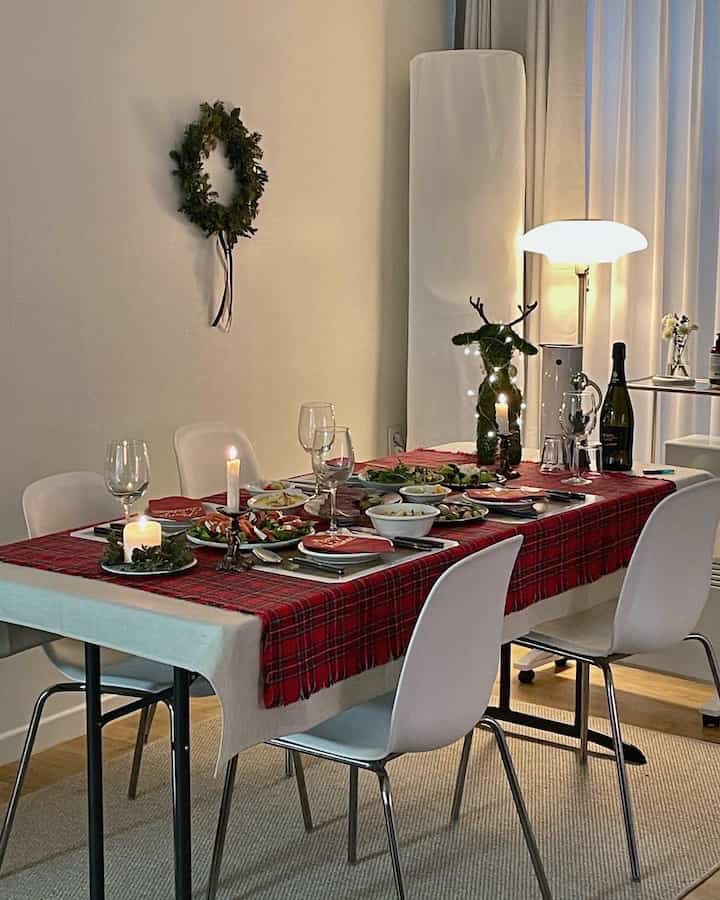 White and red toned dining room featuring a red checkered tablecloth, candles, wine glasses, and Christmas decorations for cozy home party