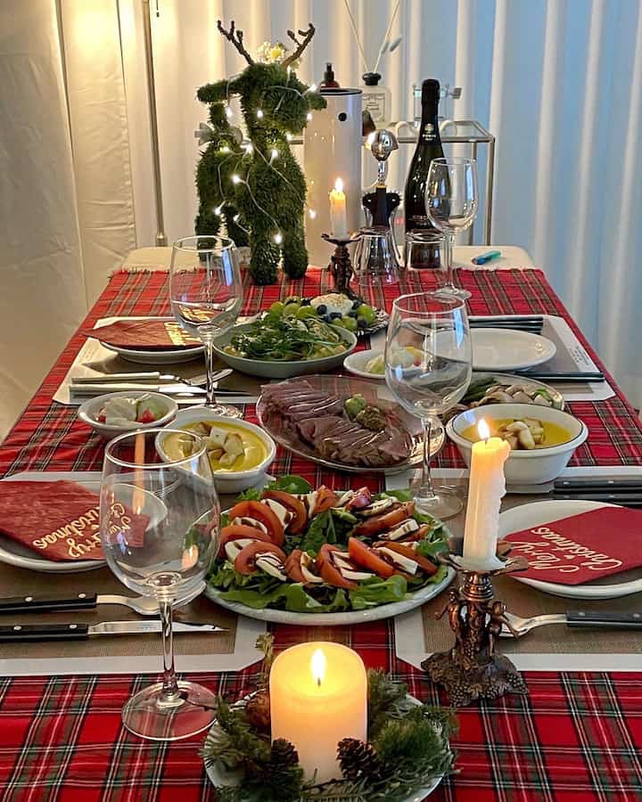 赤のチェック柄のテーブルクロスとクリスマス飾り、ワイングラスとキャンドルが配された雰囲気あるホームパーティのダイニング空間