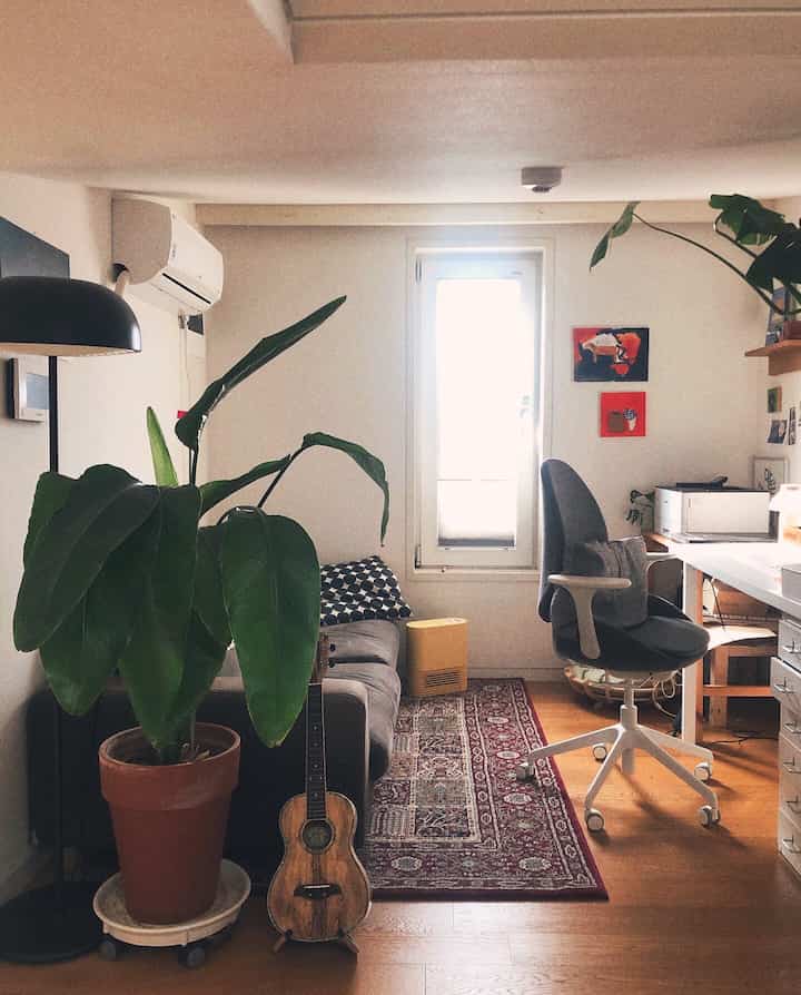 ナチュラルな色調のロフトのホームオフィス、観葉植物と快適なソファ、実用的なデスクとオフィスチェアが配置された雰囲気のあるインテリア