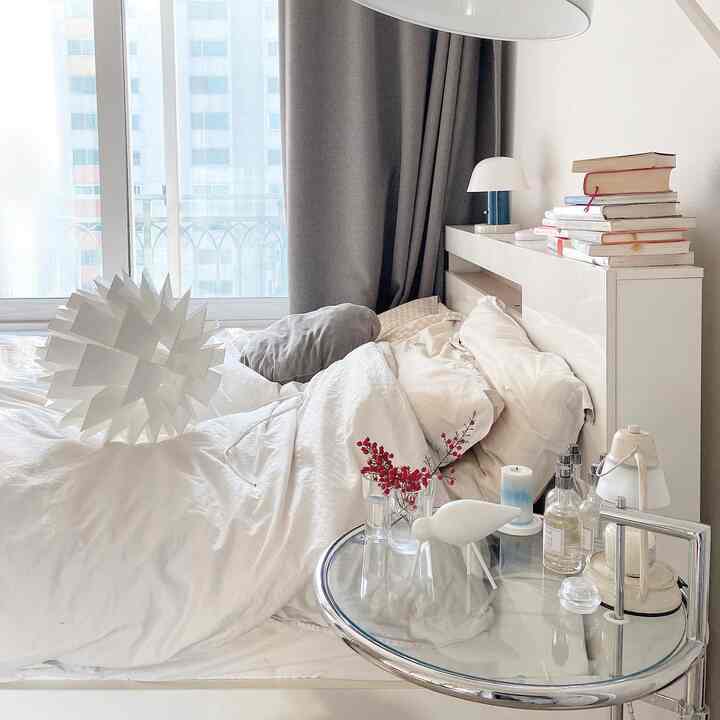 White-toned bedroom with curtains and Nordic lighting, featuring a bed and side table in a clean, cozy space