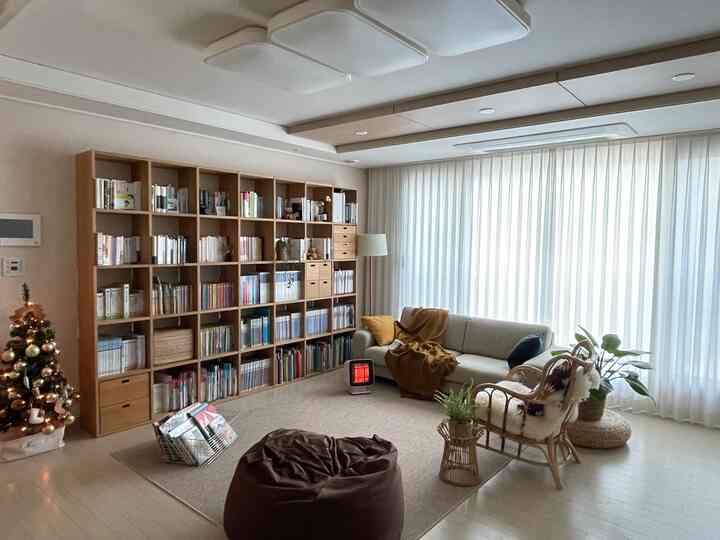 明るいベージュと木目調のリビング、広い本棚と3人掛けソファ、クリスマスツリーが調和した雰囲気のある空間