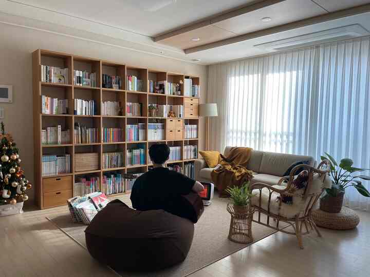 ナチュラルなベージュとブラウンのトーンのリビング、大きな本棚、ビーズクッション、ソファ、ラタンアームチェアが置かれた居心地の良い空間