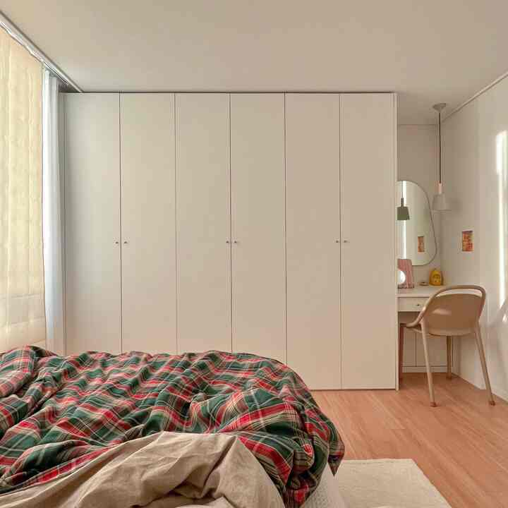 Natural-colored and white clean bedroom featuring a large built-in closet, checked duvet cover, and simple vanity setup